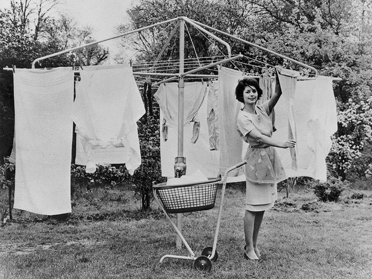 A woman hanging laundry on an early Hills rotary clothesline in a backyard